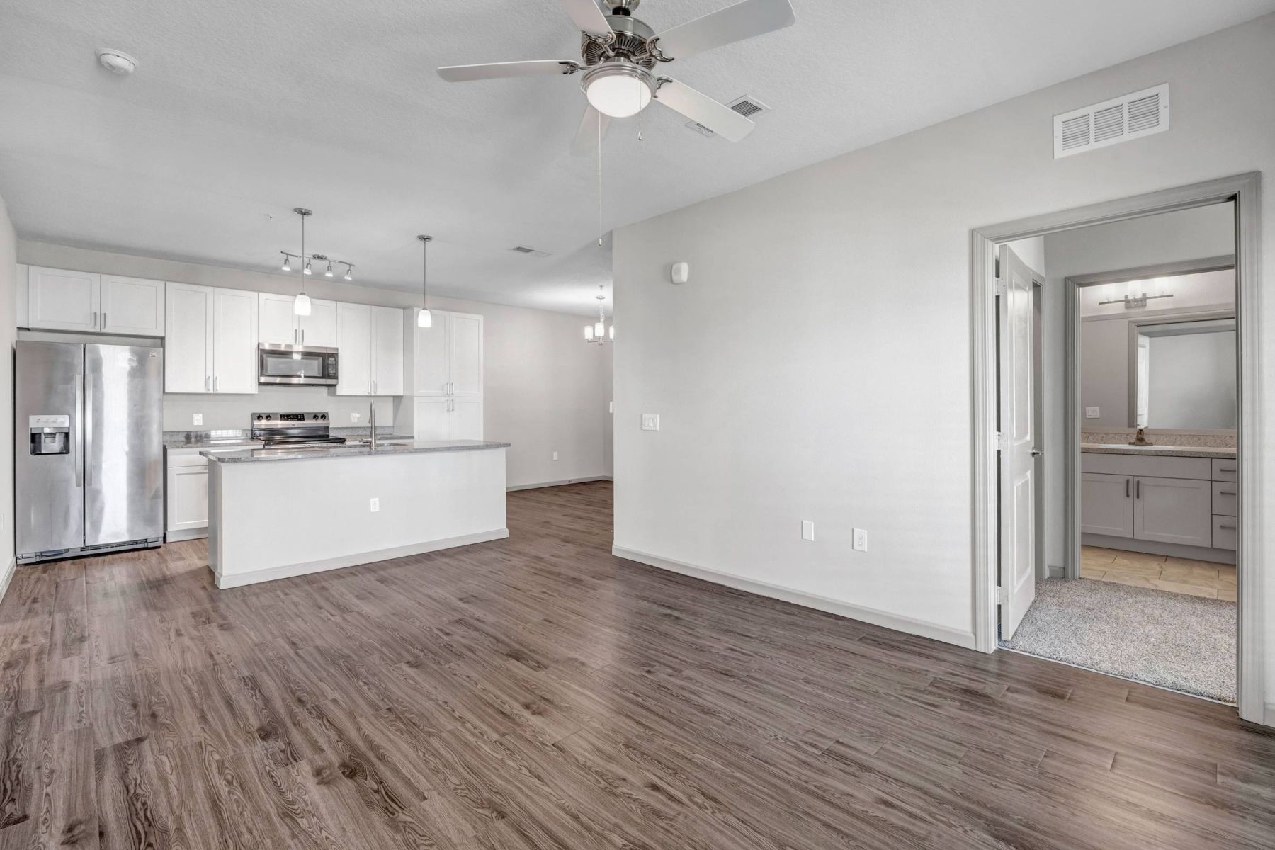 Empty room with wood floors, ceiling fan, and sliding glass door leading to a patio with vertical blinds at Apex West Midown.
